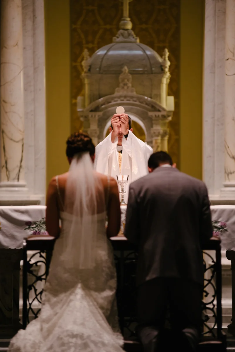 A couple kneels together at the altar during their ceremony, seen from behind.
