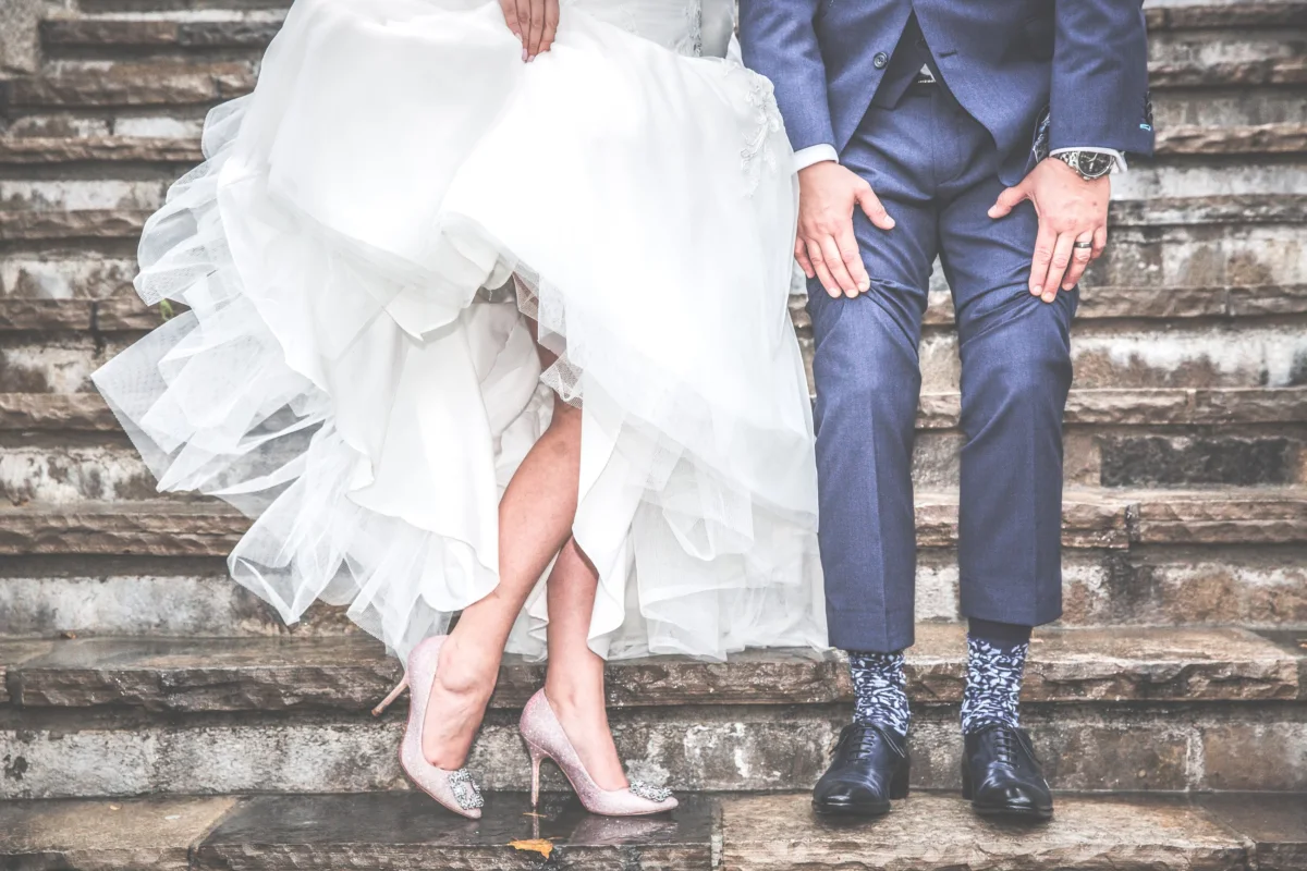 The couple sits on stone steps, a full tulle skirt beside a blue suit and patterned socks.