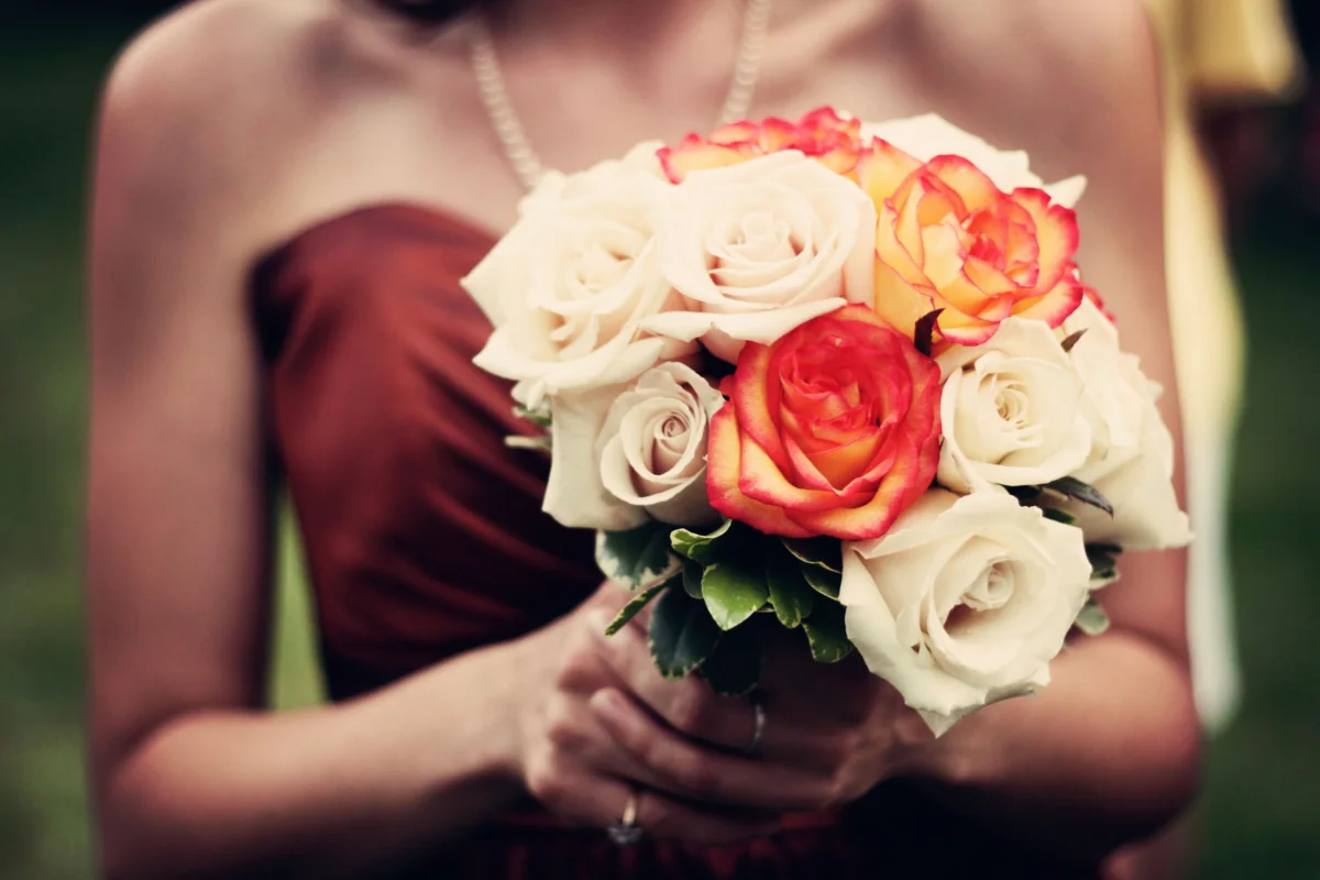 A bridesmaid in burgundy holds a bouquet of cream and coral roses.